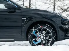 Auto nera su neve con catene sulle ruote motrici per affrontare il ghiaccio.