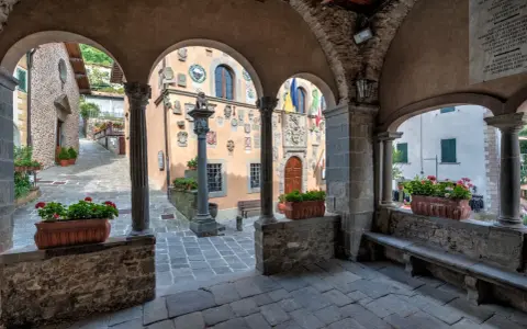 Un vicolo tra i borghi della montagna pistoiese, con archi in pietra, colonne e vasi di fiori rossi.