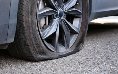 Ruota dell'auto con pneumatico sgonfio, mostra un'ernia evidente. Un problema comune che richiede attenzione immediata.