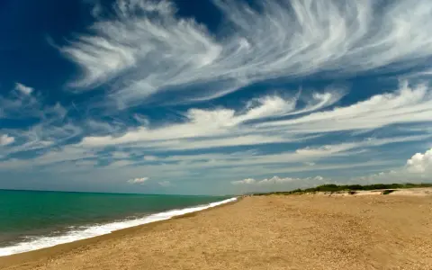 Spiaggia dorata e mare turchese al parco costiero di Rimigliano, con un cielo blu intenso solcato da nuvole bianche e leggere.