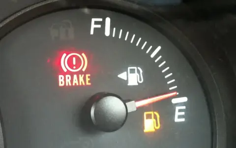 Cruscotto auto con spia freno a mano accesa e indicatore carburante quasi vuoto. È ora di fare rifornimento e resettare l'indicatore carburante.
