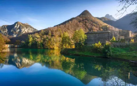Lago incantevole con riflessi di montagne e boschi autunnali. Un borgo in pietra completa il paesaggio, ideale per scoprire dove andare in montagna in Toscana.