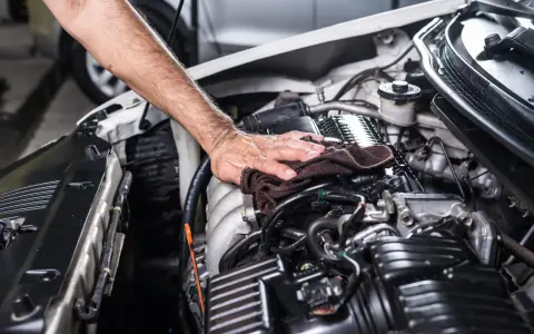 Mano che pulisce il motore dell'auto con un panno. Non è consigliabile usare l'idropulitrice per lavare il motore della macchina.