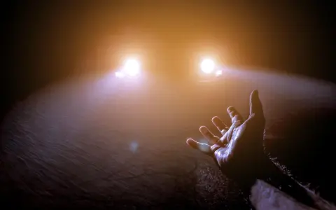 Mano tesa verso le luci abbaglianti di un'auto nella nebbia, un momento di incertezza e speranza.