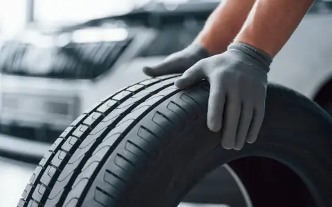 Mani guantate controllano il battistrada di uno pneumatico, valutando la sua durata gomme auto.