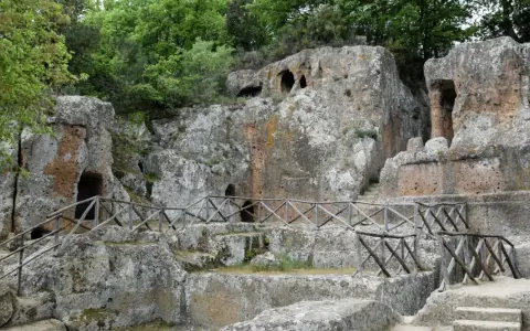 Antiche tombe scavate nella roccia, parte dei siti etruschi in Toscana, con sentieri e recinzioni in legno.