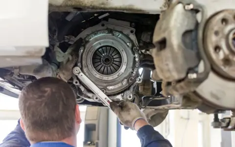 Meccanico lavora sulla frizione di un'auto. La durata della frizione varia, ma si consiglia di controllarla ogni quanti km si cambia la frizione.