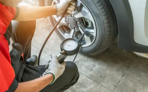 Controllo pressione gomme a caldo o freddo con manometro. Un meccanico in tuta rossa verifica la pressione degli pneumatici.