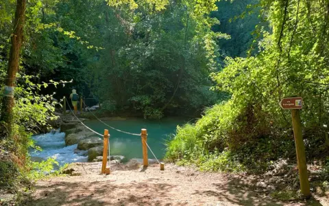 Sentiero naturalistico con guado su fiume, ideale per percorsi trekking Toscana. Segnale Via Francigena indica la direzione.