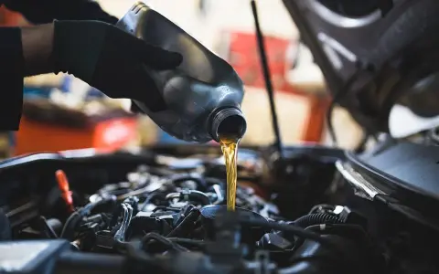 Mano con guanto versa olio motore. Il cambio olio ogni quanto è fondamentale per la salute dell'auto.