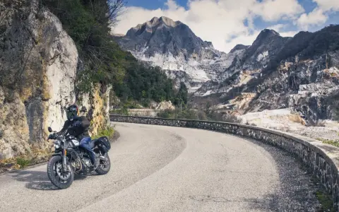 Un motociclista percorre una strada tortuosa tra le cave di marmo delle Alpi Apuane, un'avventura tra i passi toscana moto.