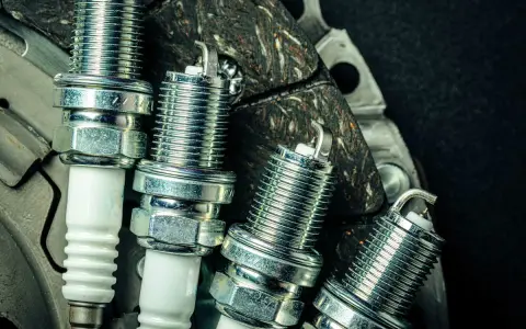 Candele auto benzina: scopri ogni quanto cambiarle per un motore efficiente. Nuove candele in primo piano su uno sfondo scuro.
