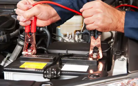 Mani che collegano i cavi alla batteria per capire come far ripartire la macchina.