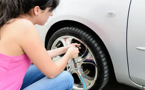 Donna controlla la pressione gomme auto estate, assicurandosi che siano gonfie al punto giusto per un viaggio sicuro.