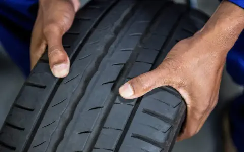 Mani che controllano il battistrada di uno pneumatico, evidenziando un insufficiente pressione di gonfiaggio degli pneumatici.