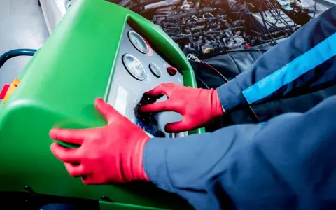 Tecnico con guanti rossi usa una macchina per controllare la perdita gas condizionatore auto.