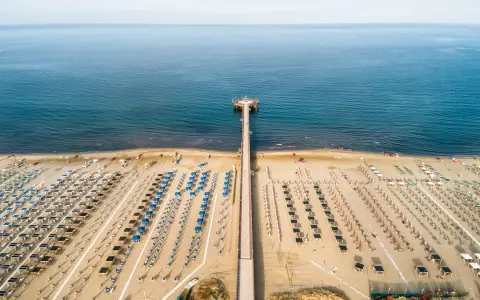 Un lungo molo si estende verso il mare calmo, con file ordinate di ombrelloni e lettini che attendono i bagnanti. Un'oasi di relax, quasi un mare vicino Firenze, dove la sabbia dorata incontra l'azzurro infinito.