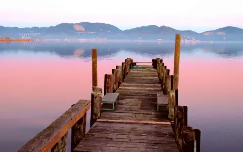 Pontile in legno su lago calmo al tramonto, con montagne sullo sfondo. Si intuisce dove si trova Torre del Lago.