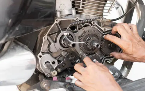 Mani che lavorano sul motore di una moto, forse per risolvere una perdita di potenza auto benzina. Ingranaggi e parti meccaniche in vista.