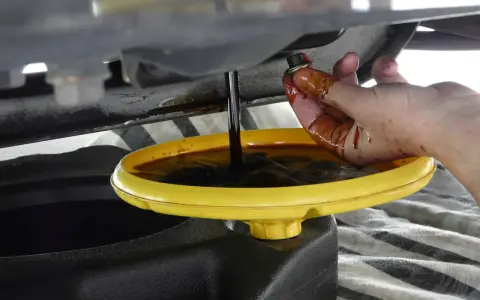 Cambio olio: un tappo sporco di olio viene tenuto da una mano mentre l'olio esausto cola in un contenitore. Forse c'era troppo olio nel motore.