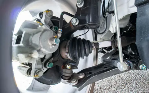 Parti della sospensione di un'auto, inclusa la pinza del freno e il giunto omocinetico con soffietto, utili per riconoscere i sintomi di un semiasse auto rotto.