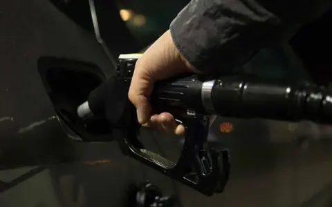 Mano che inserisce la pistola del carburante nel serbatoio dell'auto. Potrebbe indicare una pompa della benzina rotta o sintomi di malfunzionamento.