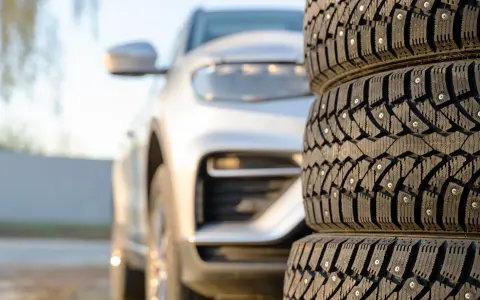 Gomme invernali con chiodi in primo piano, un'auto bianca sfocata sullo sfondo. Preparazione per l'inverno, anche se è estate.
