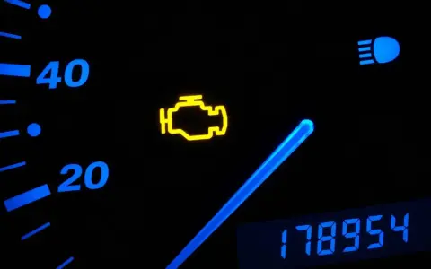 Cruscotto auto con spia motore accesa. La spia gialla a forma di motore indica un problema. Oltre, indicatori di velocità e chilometraggio.