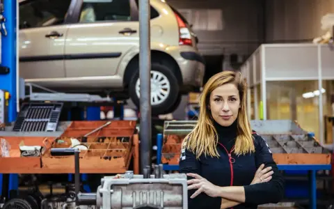 Donna in officina con auto sollevata, pronta per la manutenzione straordinaria auto.