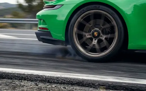 La ruota di un'auto sportiva verde lascia strisce sull'asfalto, producendo un rumore rotolamento pneumatici a bassa velocità.