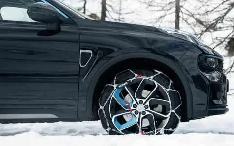 Auto nera su neve con catene sulle ruote motrici per affrontare il ghiaccio.