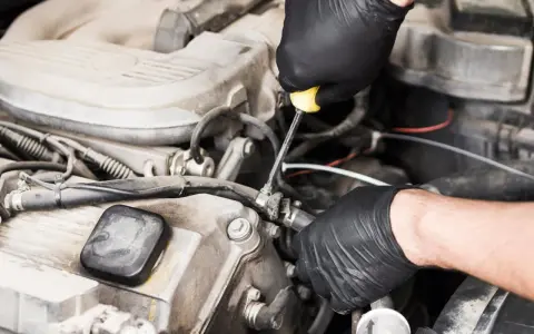 Meccanico con guanti neri lavora sul motore, risolvendo problemi pompa gasolio serbatoio.