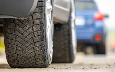 Primo piano di pneumatici invernali, con un'altra auto in lontananza. La classe rumorosità pneumatici è un fattore importante per il comfort di guida.