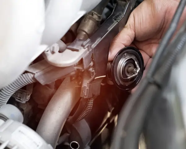 Mano che rimuove il termostato dell'auto. Un bulbo radiatore rotto può causare surriscaldamento.