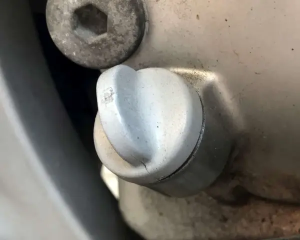 Dettaglio di un tappo motore con una piccola crepa, suggerendo una possibile fuoriuscita olio motore dal tappo.