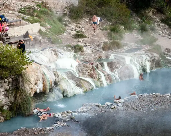 Persone si rilassano nelle calde acque delle terme di Petriolo libere, tra rocce e vegetazione.