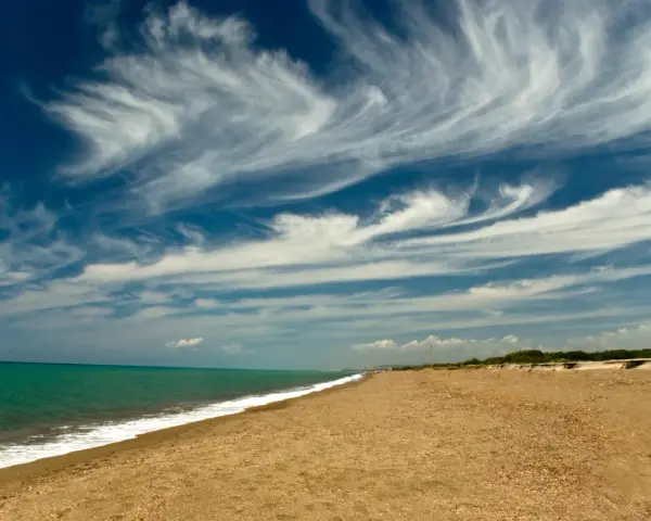 Spiaggia dorata e mare turchese al parco costiero di Rimigliano, con un cielo blu intenso solcato da nuvole bianche e leggere.