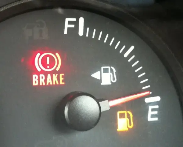 Cruscotto auto con spia freno a mano accesa e indicatore carburante quasi vuoto. È ora di fare rifornimento e resettare l'indicatore carburante.