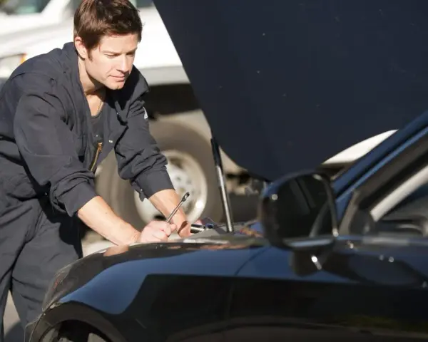 Meccanico in tuta blu lavora sul motore di un'auto nera. La revisione auto si può fare in tutta Italia, ovunque ci sia un professionista.