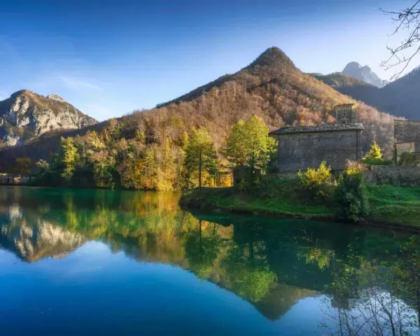 Lago incantevole con riflessi di montagne e boschi autunnali. Un borgo in pietra completa il paesaggio, ideale per scoprire dove andare in montagna in Toscana.