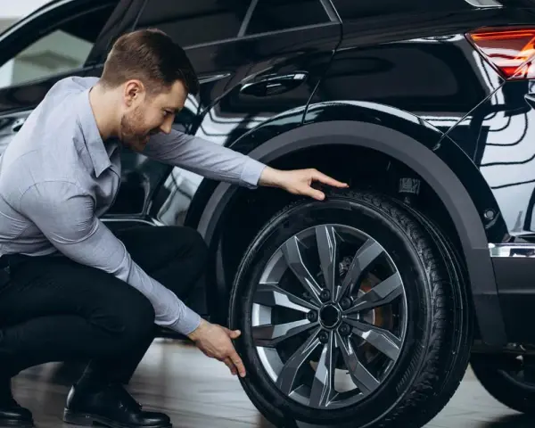 Uomo in ginocchio effettua il controllo gomme auto, esaminando il battistrada del pneumatico nero.