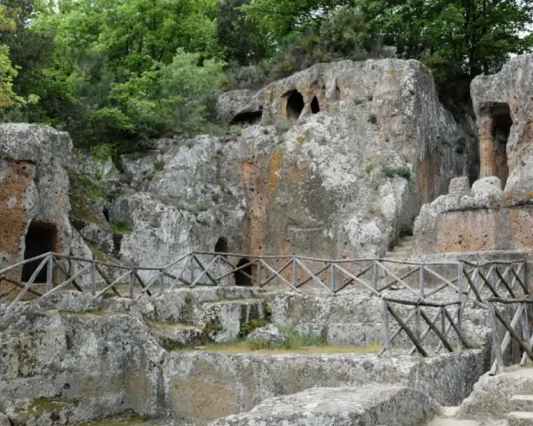 Antiche tombe scavate nella roccia, parte dei siti etruschi in Toscana, con sentieri e recinzioni in legno.