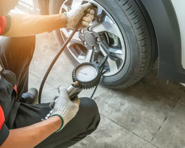 Controllo pressione gomme a caldo o freddo con manometro. Un meccanico in tuta rossa verifica la pressione degli pneumatici.