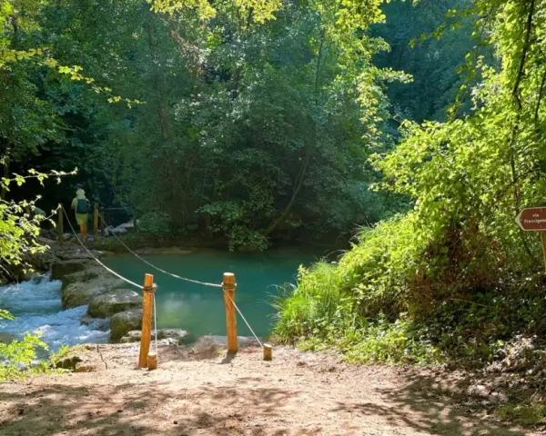 Sentiero naturalistico con guado su fiume, ideale per percorsi trekking Toscana. Segnale Via Francigena indica la direzione.