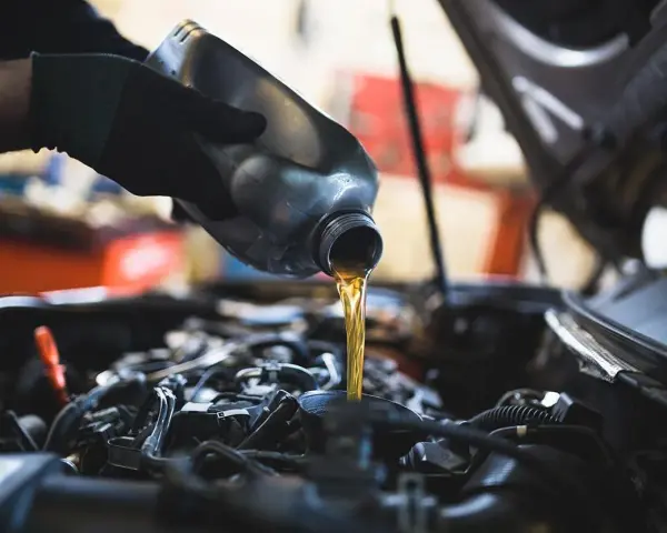 Mano con guanto versa olio motore. Il cambio olio ogni quanto è fondamentale per la salute dell'auto.