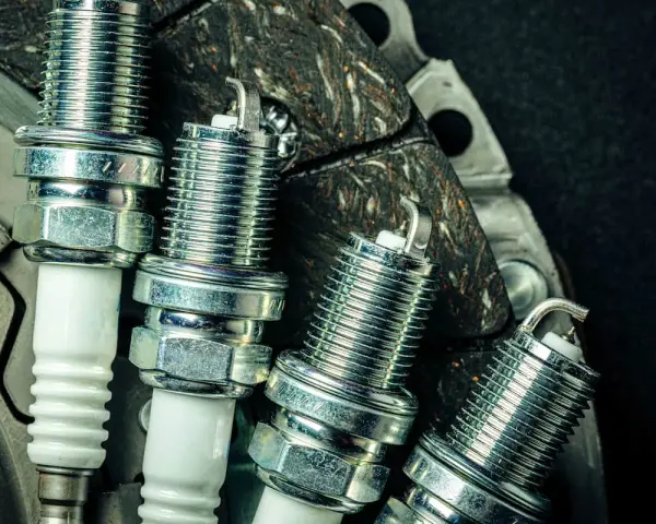 Candele auto benzina: scopri ogni quanto cambiarle per un motore efficiente. Nuove candele in primo piano su uno sfondo scuro.