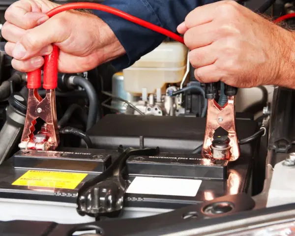 Mani che collegano i cavi alla batteria per capire come far ripartire la macchina.