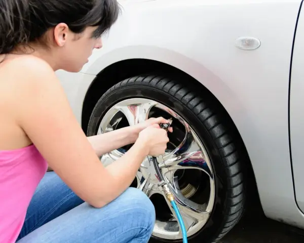 Donna controlla la pressione gomme auto estate, assicurandosi che siano gonfie al punto giusto per un viaggio sicuro.