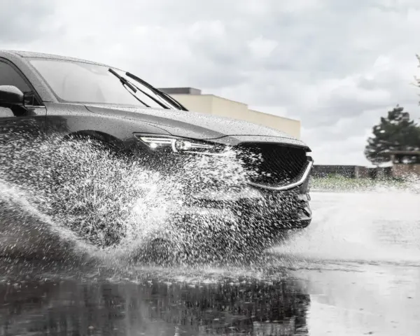 Un'auto scura attraversa una pozzanghera, sollevando un'enorme onda d'acqua. Il fenomeno dell'aquaplaning aumenta con la pioggia.