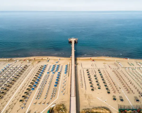 Un lungo molo si estende verso il mare calmo, con file ordinate di ombrelloni e lettini che attendono i bagnanti. Un'oasi di relax, quasi un mare vicino Firenze, dove la sabbia dorata incontra l'azzurro infinito.